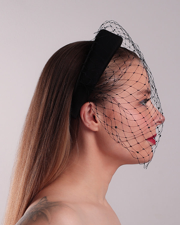 Model is showcasing the right side of a black high headband embellished with a black veil, adorned with black crystals.