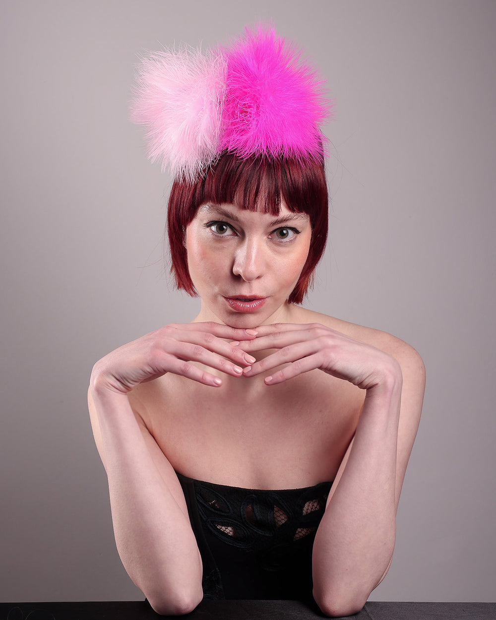 The model showcases the front of the NYX that is crafted on a hot pink satin headband. This playful fascinator features two pom-pom clouds of marabou feathers in graduated shades of candy pink and fuchsia. Designed by Merve Bayindir.