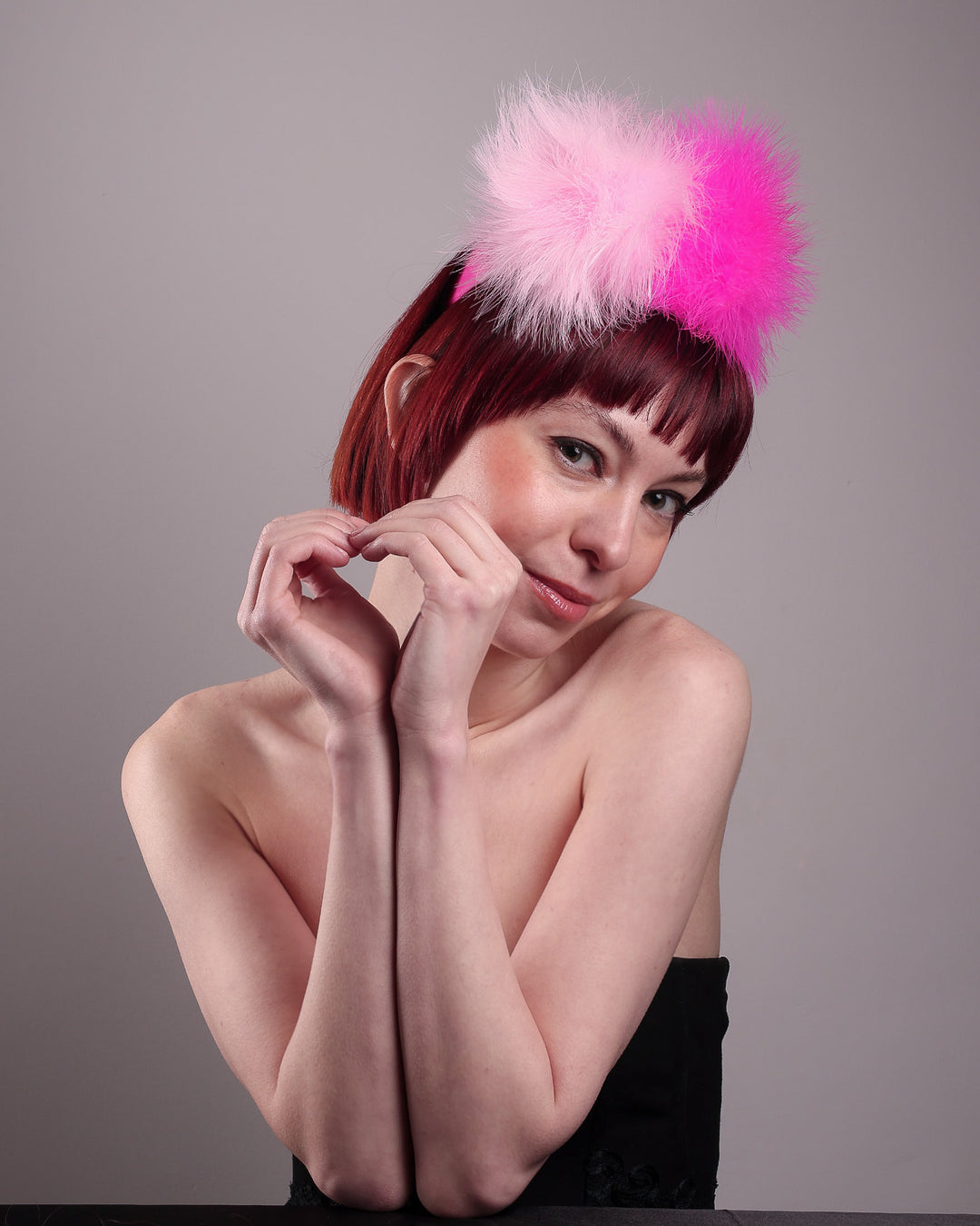 The model showcases the right front of the NYX that is crafted on a hot pink satin headband. This playful fascinator features two pom-pom clouds of marabou feathers in graduated shades of candy pink and fuchsia. Designed by Merve Bayindir.