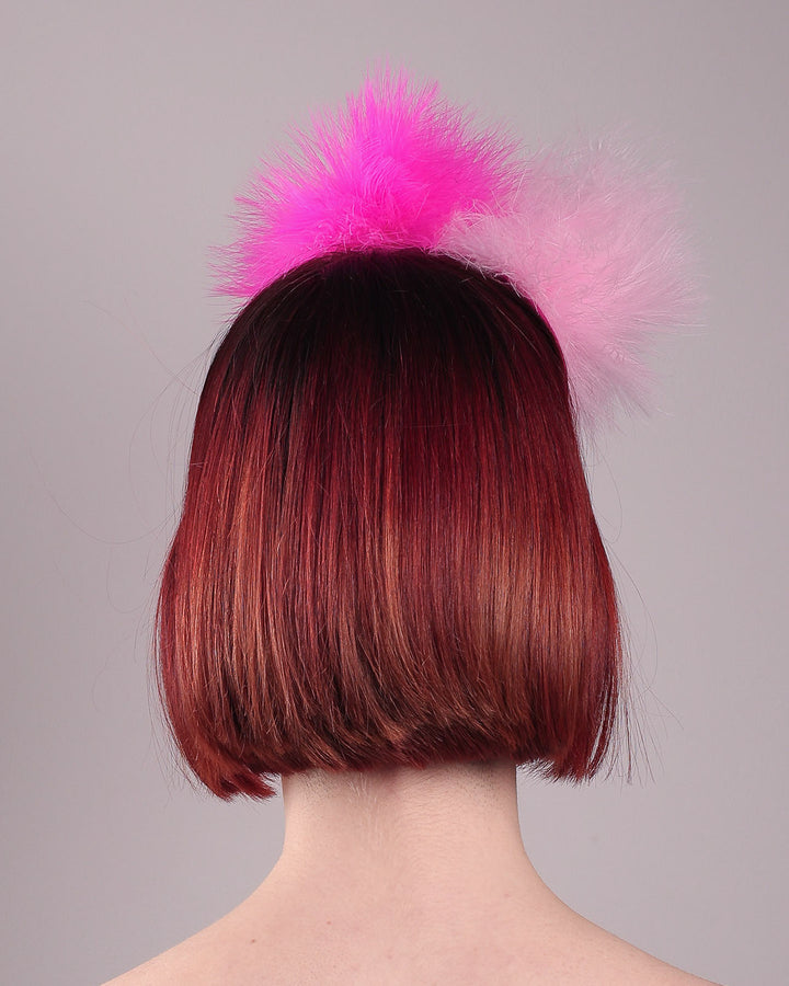 The model showcases the back of the NYX that is crafted on a hot pink satin headband. This playful fascinator features two pom-pom clouds of marabou feathers in graduated shades of candy pink and fuchsia. Designed by Merve Bayindir.