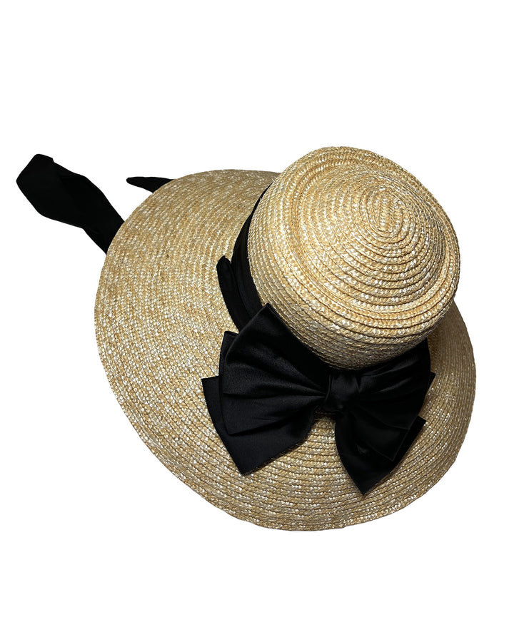 Natural woven straw wide brim boater hat with a wide brim, wrapped in a black ribbon and finished with an oversized black satin bow at the side. Designed and made by Merve Bayindir Millinery.
