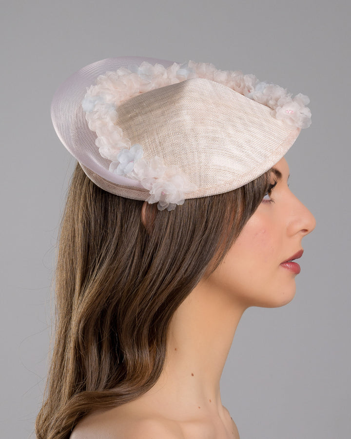The model is showcasing the right side close up of the blush pink sinamay fascinator with a soft oval crown, trimmed with delicate pastel chiffon flowers and finished with a sheer pale veil overlay, mounted on a slim black headband. Designed and made by Merve Bayindir Millinery.
