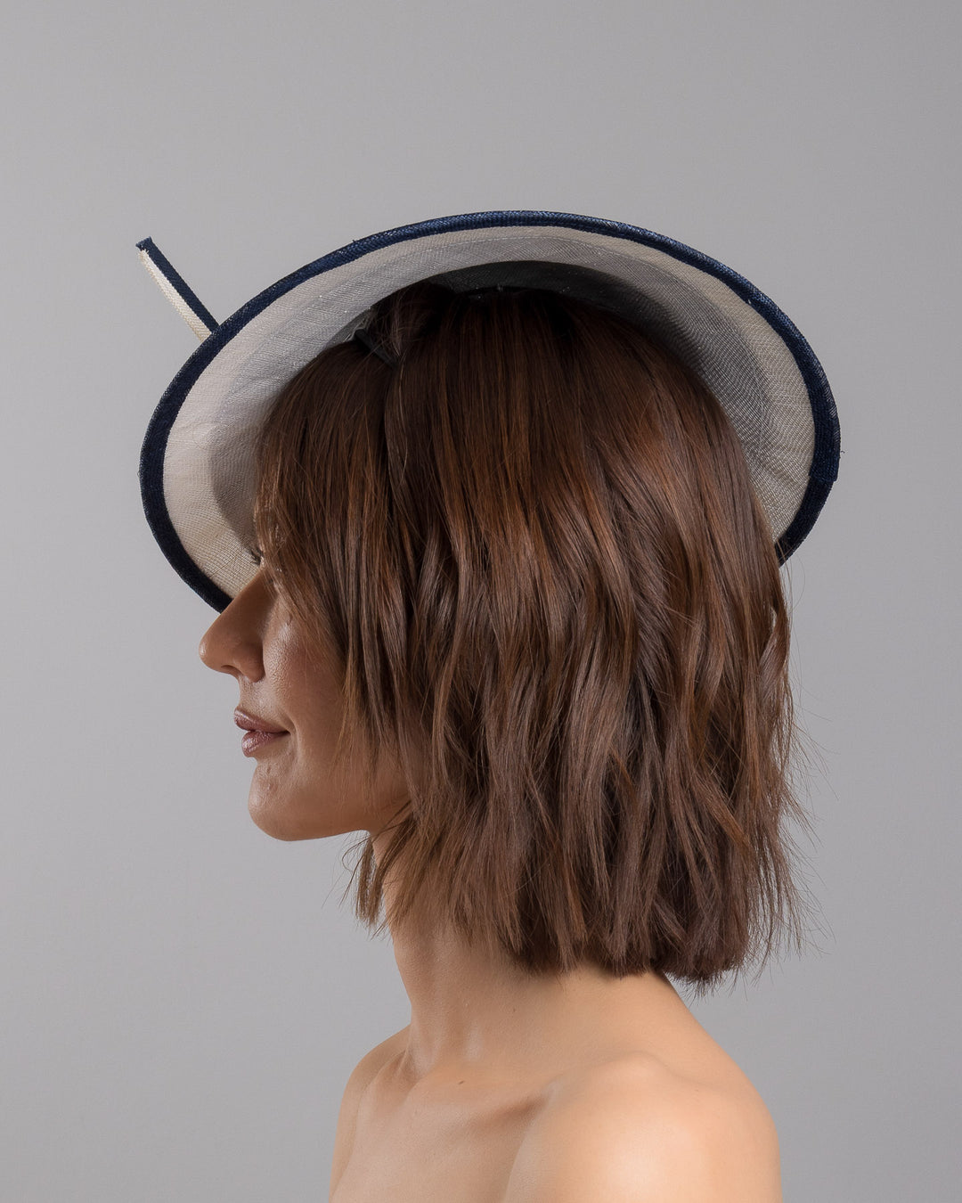 Model is showcasing the left side close up of multi layered tear drop shaped saucer in navy and white. This wide brim hat is decorated with navy and white buntal stripes and multi coloured crystal embellishments on the front. Designed and made by Merve Bayindir millinery.