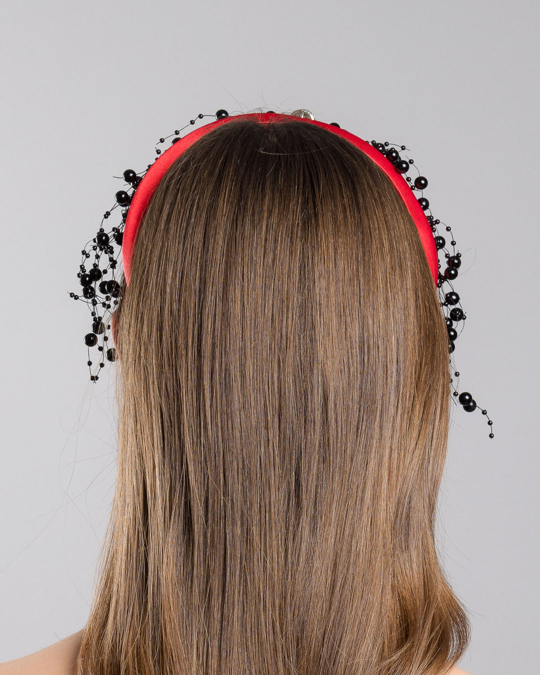 Model showcasing the back side close up of bright red silk sateen headband, decorated with crystal embellish octopus brooch and multi size black loose beads. Made by Merve Bayindir Millinery.