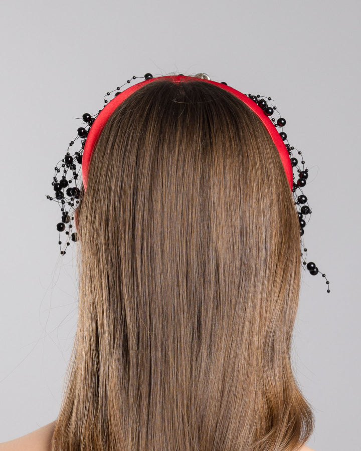 Model showcasing the back side close up of bright red silk sateen headband, decorated with crystal embellish octopus brooch and multi size black loose beads. Made by Merve Bayindir Millinery.
