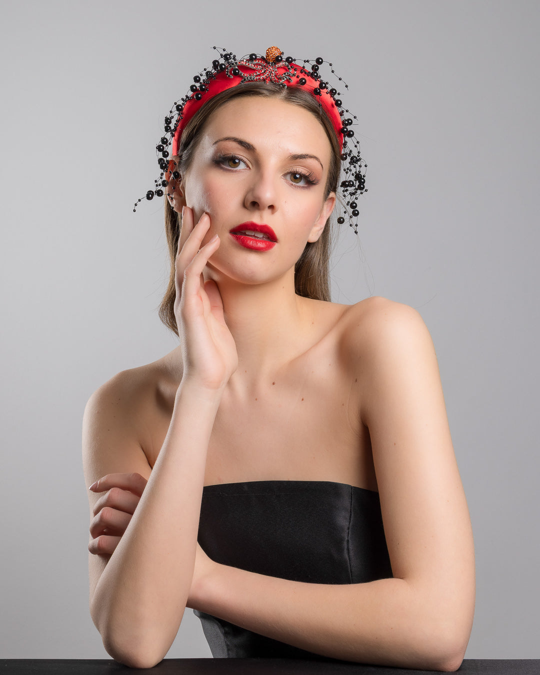 Female model wearing Octopus the bright red silk sateen headband, decorated with crystal embellish octopus brooch and multi size black loose beads. Made by Merve Bayindir Millinery.