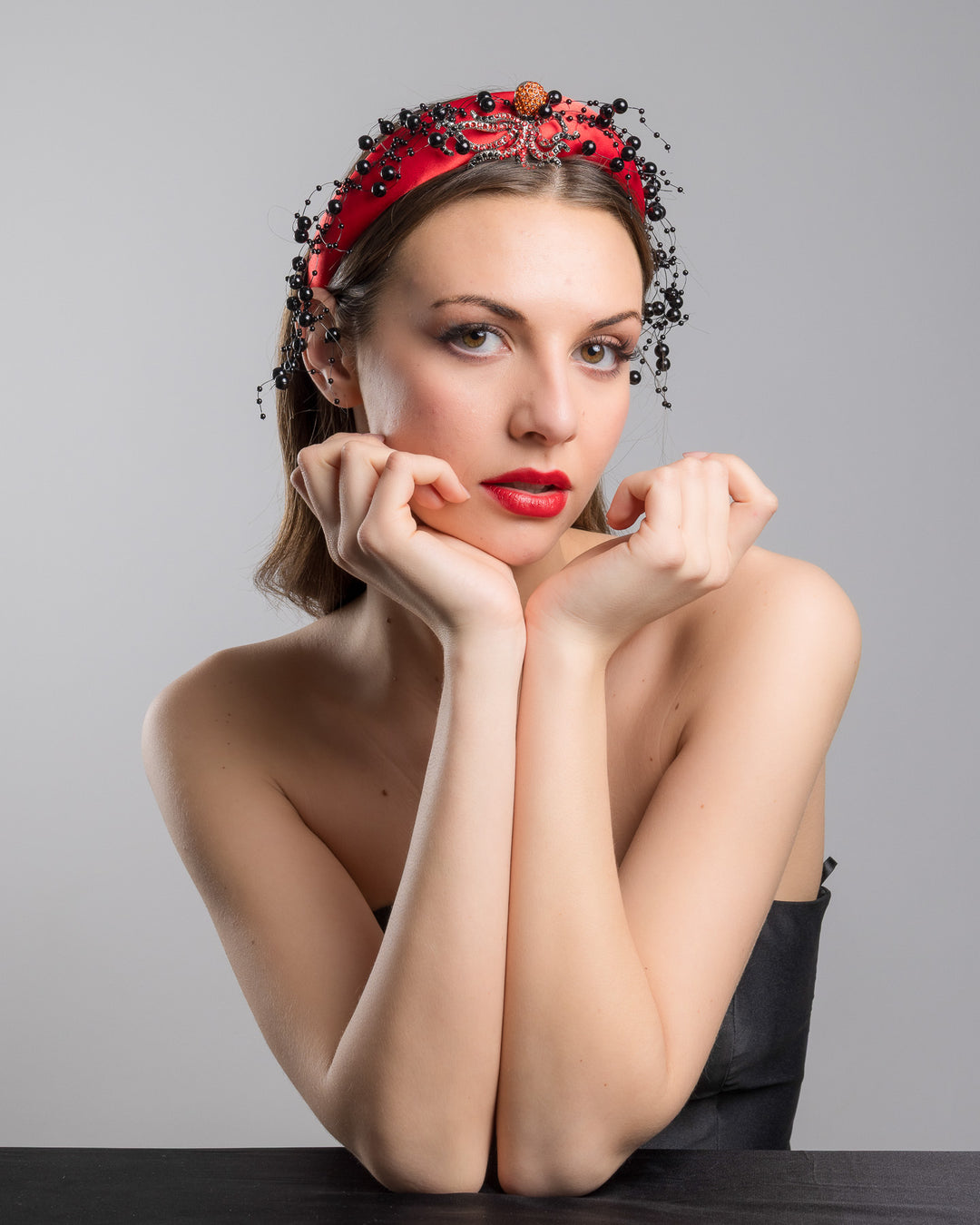 Female model wearing Octopus the bright red silk sateen headband, decorated with crystal embellish octopus brooch and multi size black loose beads. Made by Merve Bayindir Millinery.