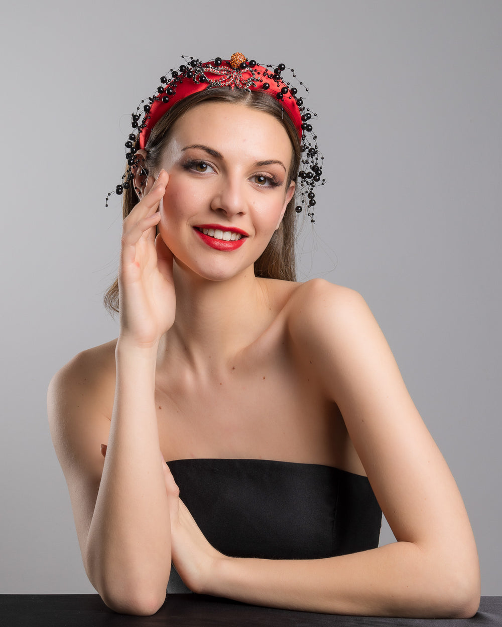Female model wearing Octopus the bright red silk sateen headband, decorated with crystal embellish octopus brooch and multi size black loose beads. Made by Merve Bayindir Millinery.