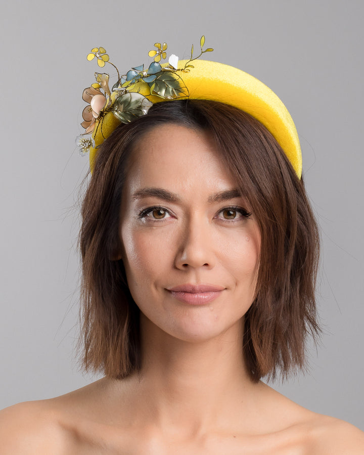 Model showcasing the front of high yellow velvet luxury headband decorated with medium sized multi colour resin flower bouquet, made by Merve Bayindir Millinery.
