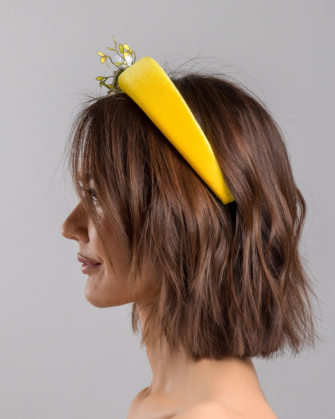 Model showcasing the left side of high yellow velvet luxury headband decorated with medium sized multi colour resin flower bouquet, made by Merve Bayindir Millinery.