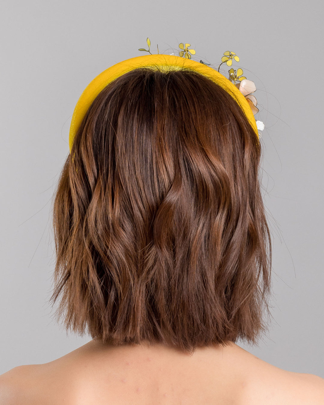 Model showcasing the back of high yellow velvet luxury headband decorated with medium sized multi colour resin flower bouquet, made by Merve Bayindir Millinery.