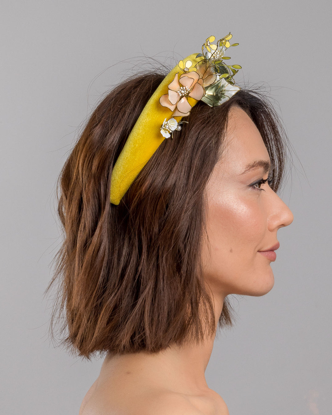 Model showcasing the right side of high yellow velvet luxury headband decorated with medium sized multi colour resin flower bouquet, made by Merve Bayindir Millinery.