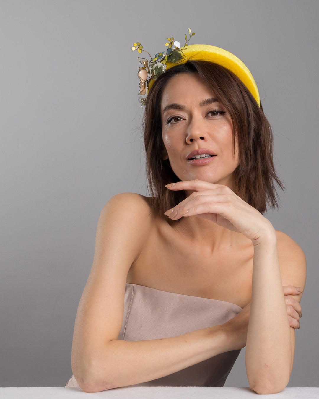Model posing, wearing Officium high yellow velvet luxury headband decorated with medium sized multi colour resin flower bouquet, made by Merve Bayindir Millinery.