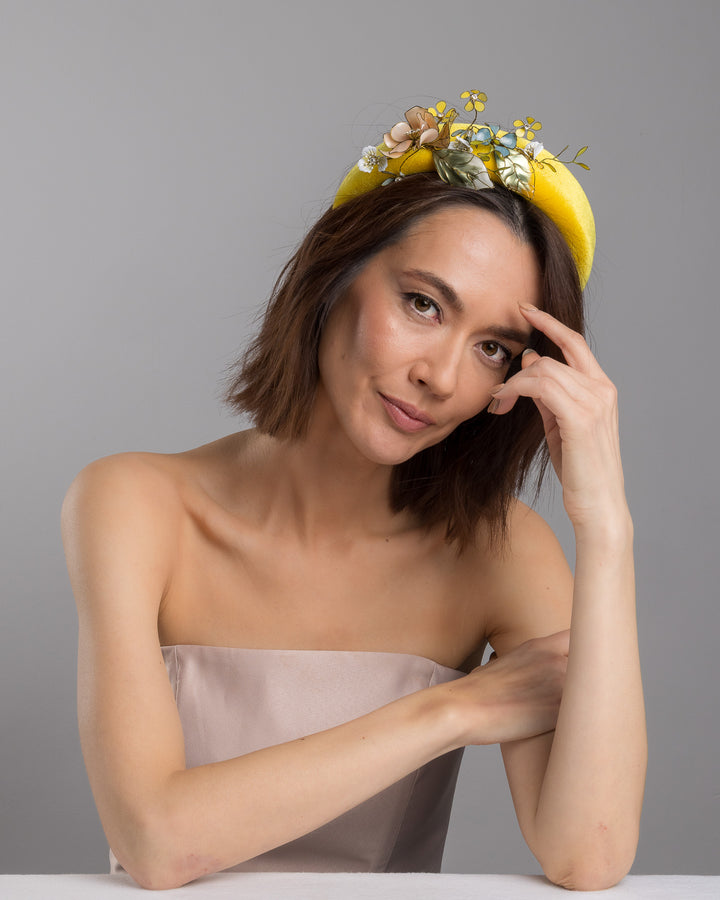 Model posing, wearing Officium high yellow velvet luxury headband decorated with medium sized multi colour resin flower bouquet, made by Merve Bayindir Millinery.