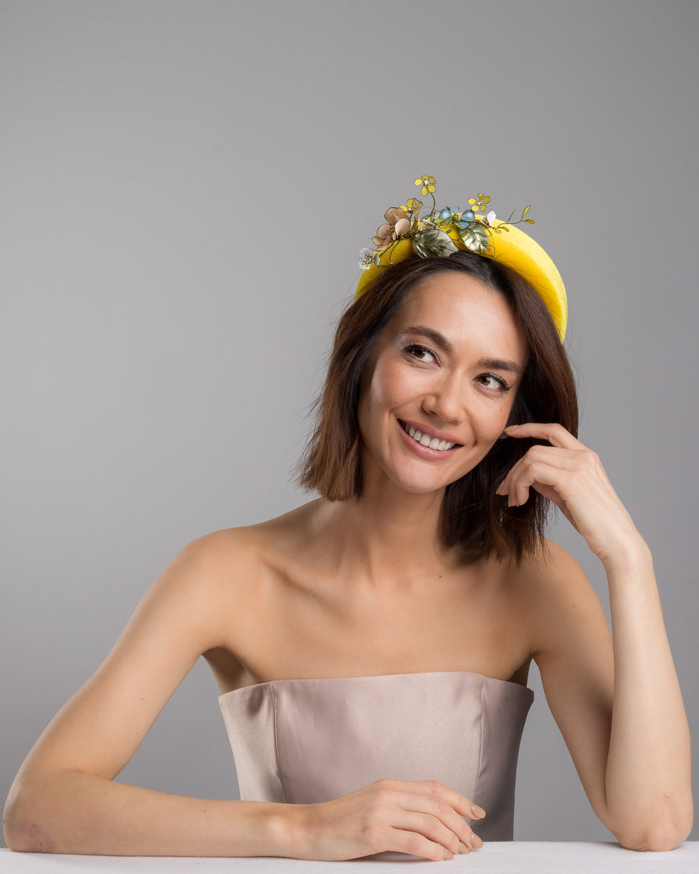 Model posing, wearing Officium high yellow velvet luxury headband decorated with medium sized multi colour resin flower bouquet, made by Merve Bayindir Millinery.