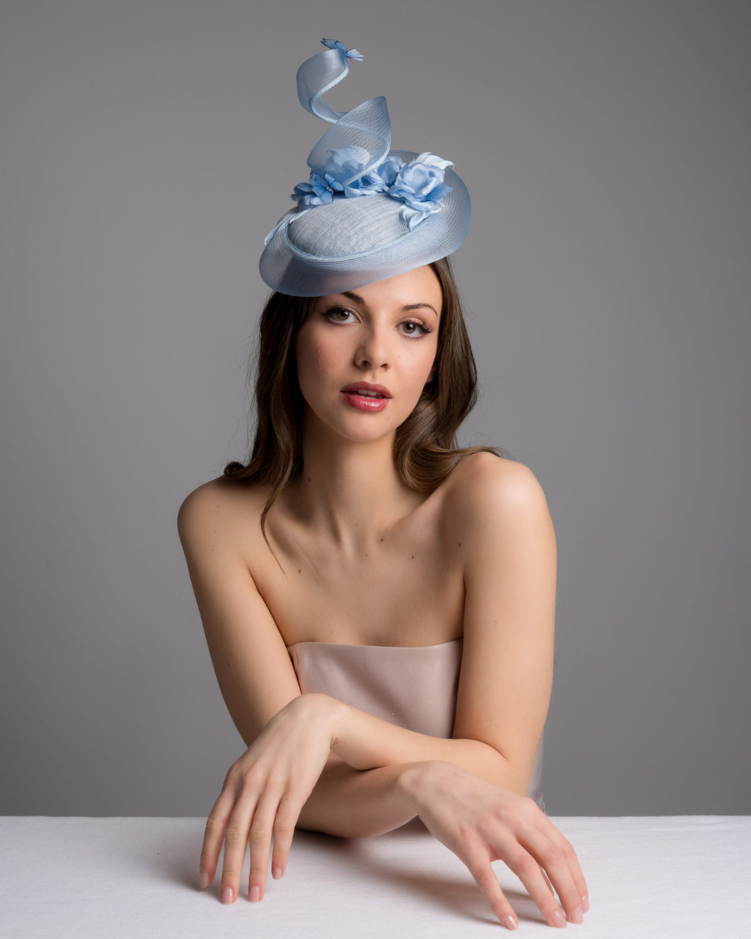 The  female model is posing, wearing Onyx,the light blue button shaped fascinator. This unique fascinator is circled with light blue crinoline and is decorated with blue roses, shaded blue leaves and blue organza butterflies. Designed and made by Merve Bayindir Millinery.
