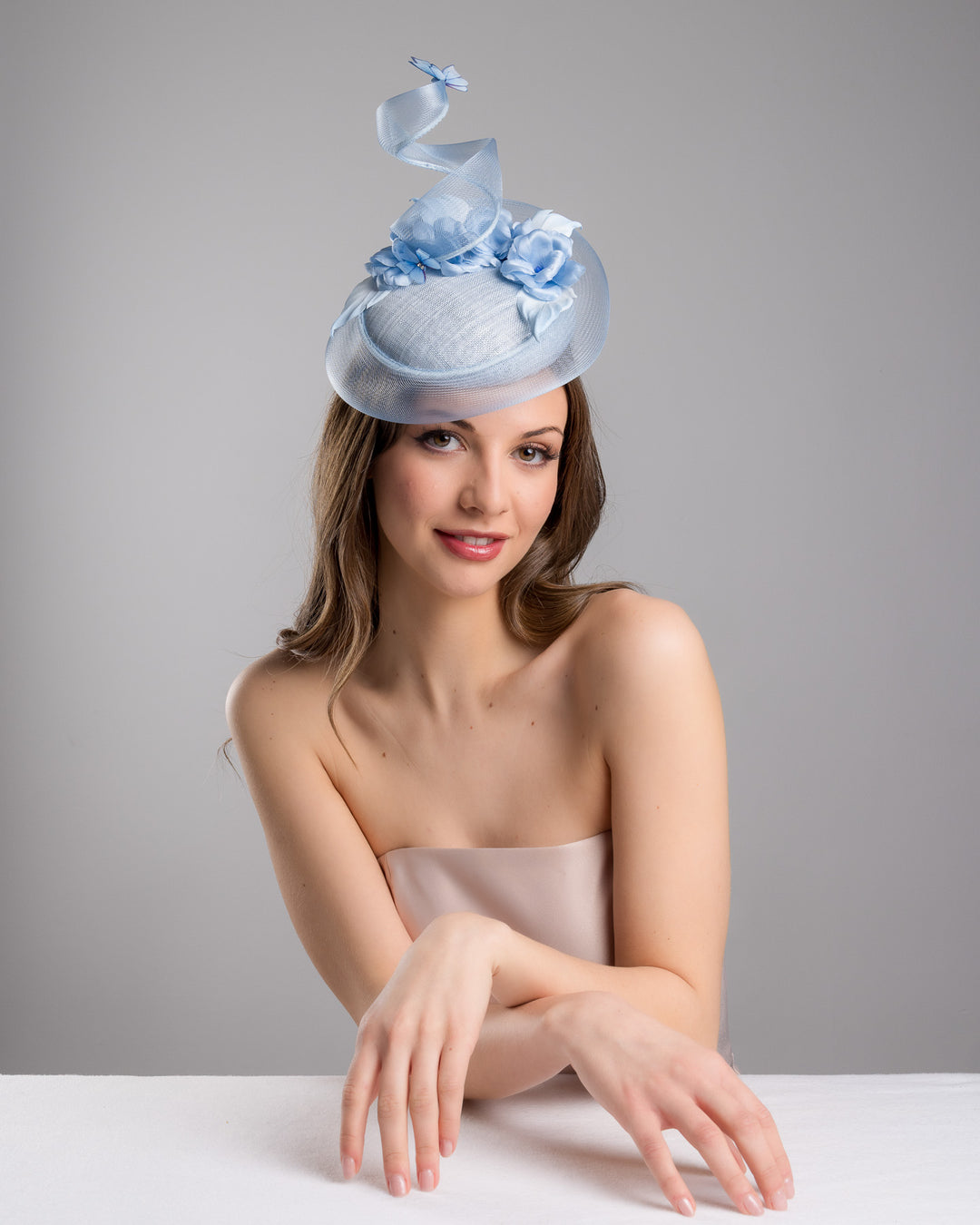 The  female model is posing, wearing Onyx,the light blue button shaped fascinator. This unique fascinator is circled with light blue crinoline and is decorated with blue roses, shaded blue leaves and blue organza butterflies. Designed and made by Merve Bayindir Millinery.
