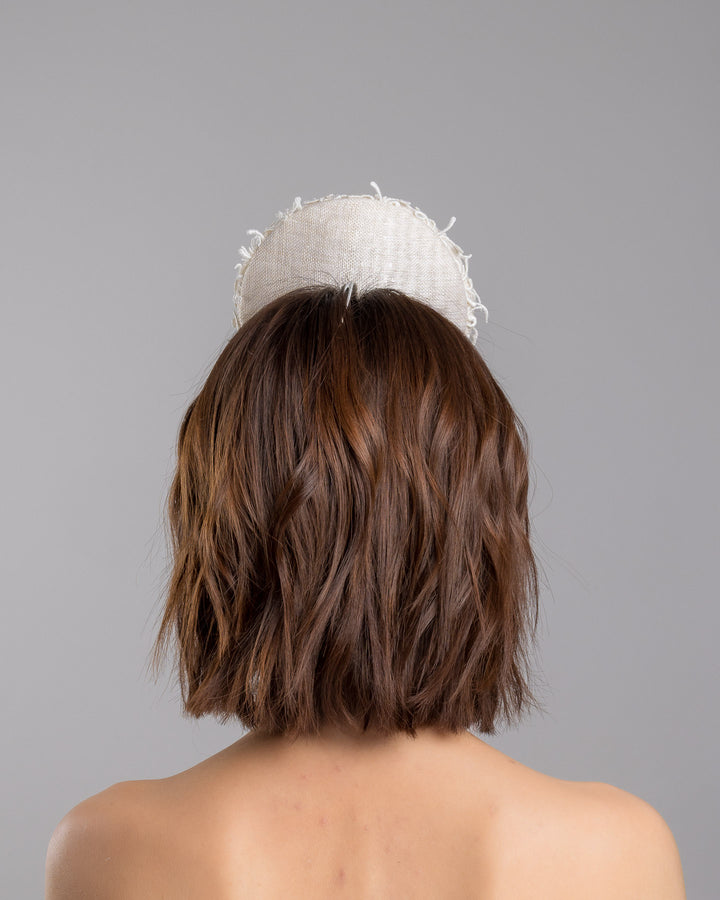 Model is showcasing the back side close up of double sided, white high top button style fascinator covered with sequins and lace with embroidered 3D swirls. Positioned on the top front centre of the head. Designed and made by Merve Bayindir Millinery.