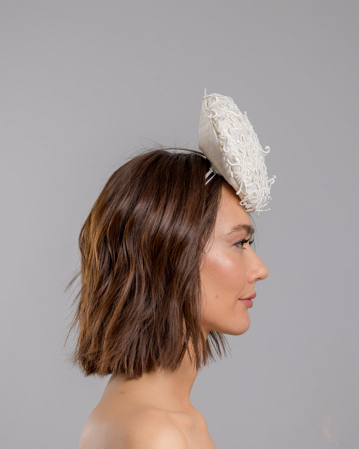 Model is showcasing the right side close up of double sided, white high top button style fascinator covered with sequins and lace with embroidered 3D swirls. Positioned on the top front centre of the head. Designed and made by Merve Bayindir Millinery.