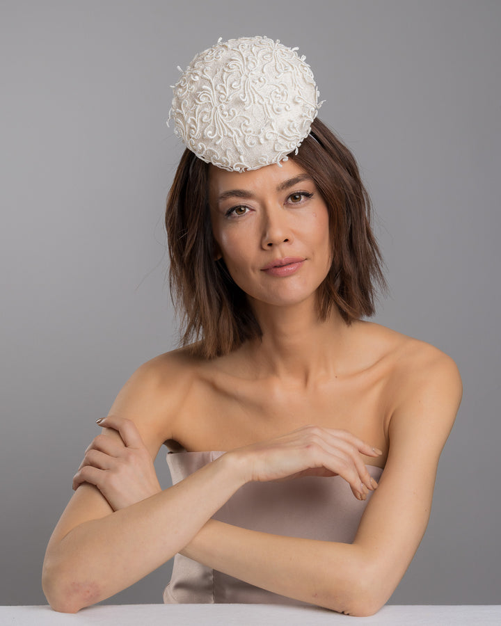 Model is posing wearing Ophelia the double sided, white high top button style fascinator covered with sequins and lace with embroidered 3D swirls. Positioned on the top front centre of the head. Designed and made by Merve Bayindir Millinery.