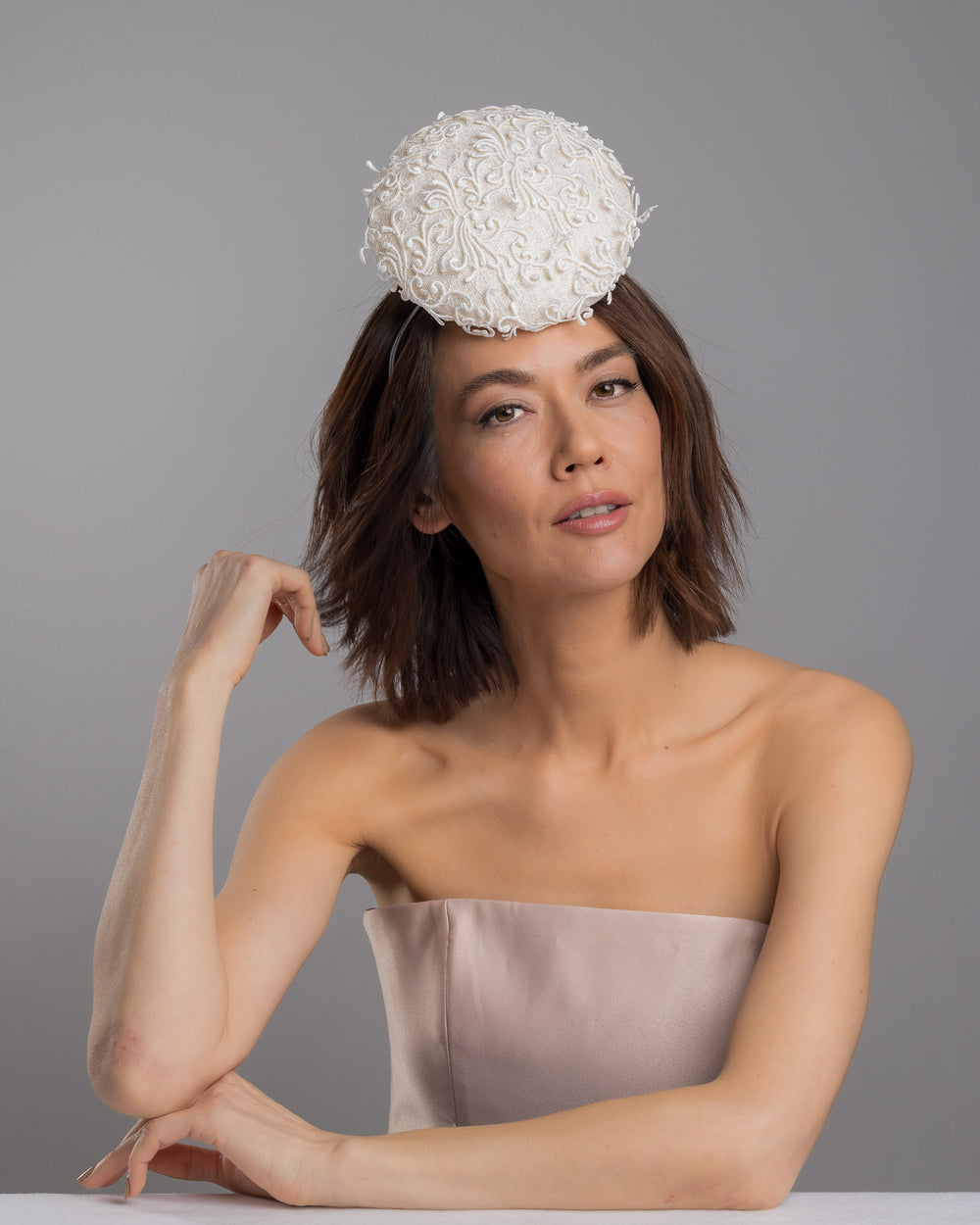 Model is posing wearing Ophelia the double sided, white high top button style fascinator covered with sequins and lace with embroidered 3D swirls. Positioned on the top front centre of the head. Designed and made by Merve Bayindir Millinery.