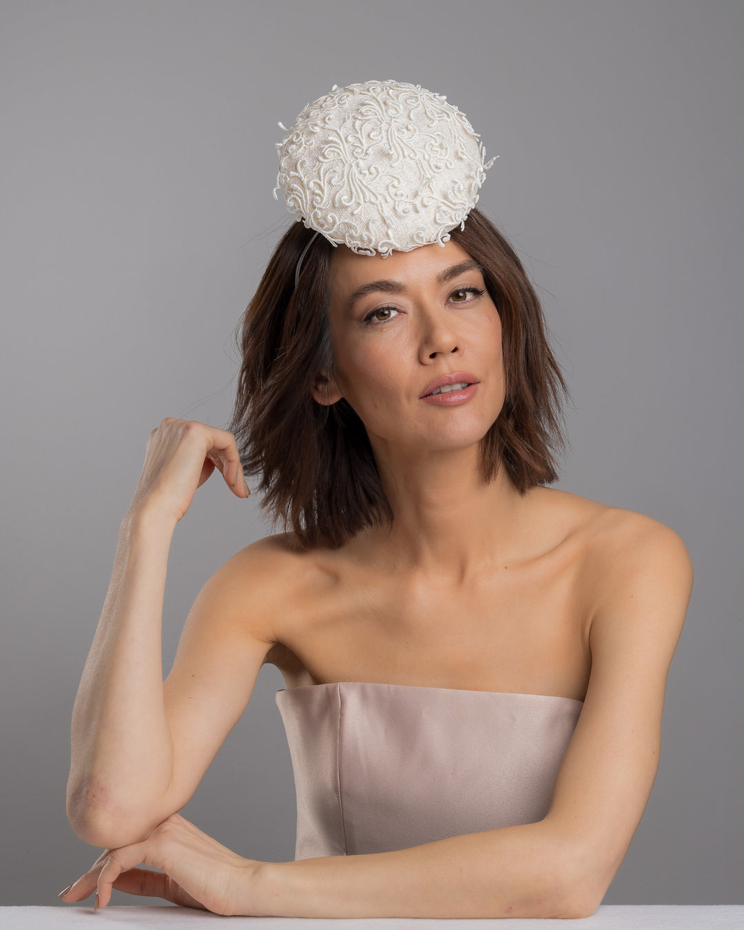 Model is posing wearing Ophelia the double sided, white high top button style fascinator covered with sequins and lace with embroidered 3D swirls. Positioned on the top front centre of the head. Designed and made by Merve Bayindir Millinery.