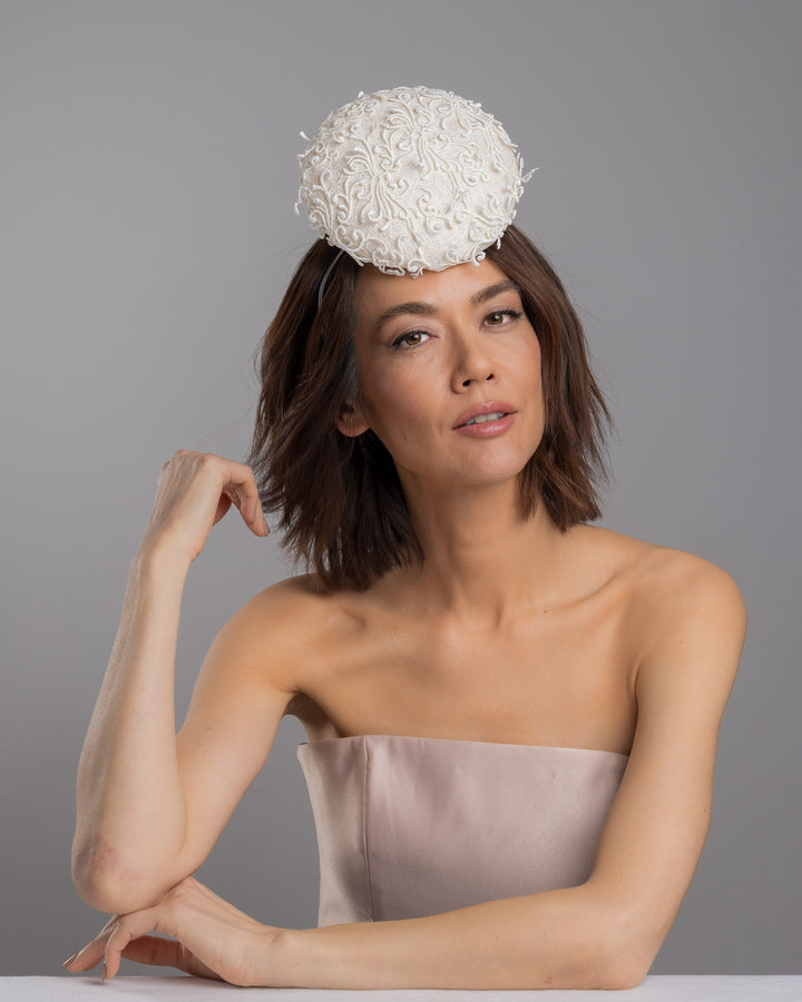 Model is posing wearing Ophelia the double sided, white high top button style fascinator covered with sequins and lace with embroidered 3D swirls. Positioned on the top front centre of the head. Designed and made by Merve Bayindir Millinery.