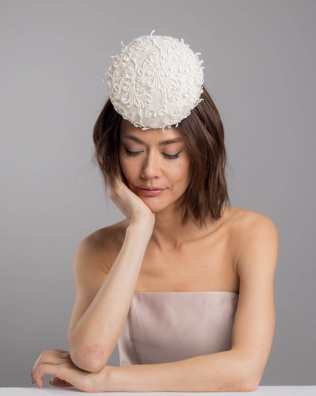 Model is posing wearing Ophelia the double sided, white high top button style fascinator covered with sequins and lace with embroidered 3D swirls. Positioned on the top front centre of the head. Designed and made by Merve Bayindir Millinery.