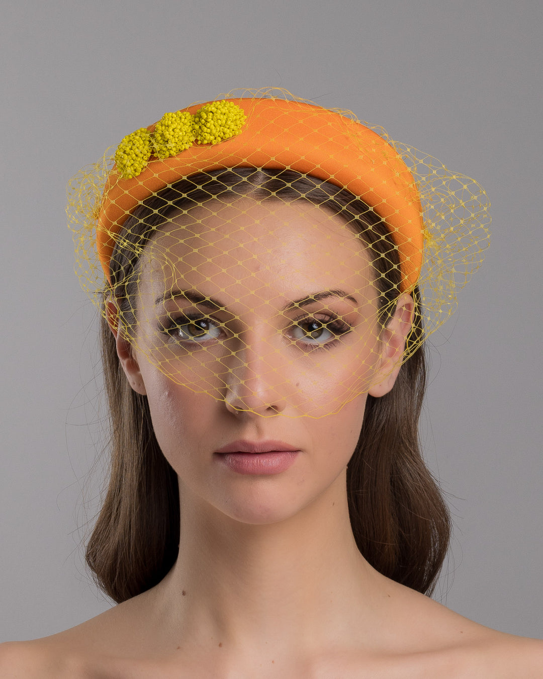 Model is showcasing the front side close up of high orange headband with yellow veil, and three yellow bead cluster. Made by Merve Bayindir Millinery.