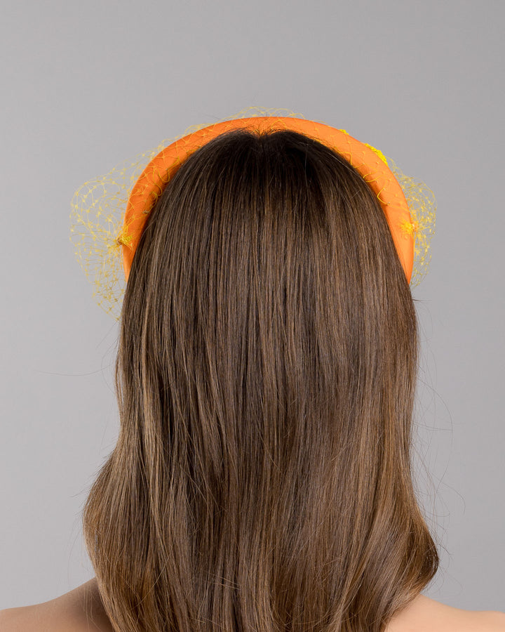 Model is showcasing the back side close up of high orange headband with yellow veil, and three yellow bead cluster. Made by Merve Bayindir Millinery.