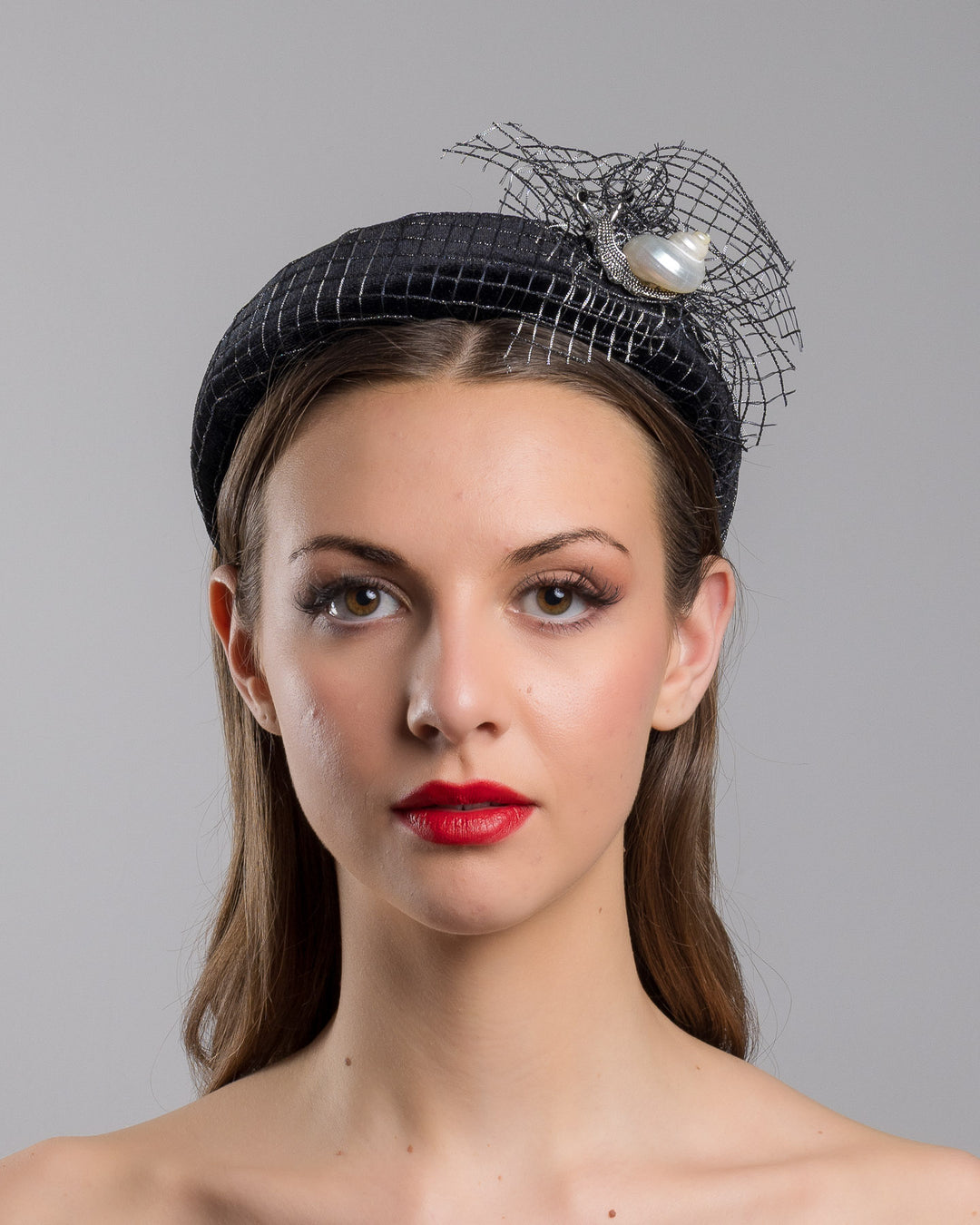 Model is showcasing the front side close up of Black Velvet High Headband, covered with a silver black mix net fabric. It is embellished with a net fabric flower and a mother of pearl detailed snail brooch. Made by Merve Bayindir Millinery.