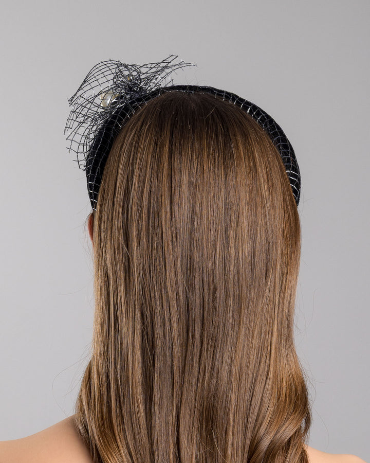 Model is showcasing the back side close up of Black Velvet High Headband, covered with a silver black mix net fabric. It is embellished with a net fabric flower and a mother of pearl detailed snail brooch. Made by Merve Bayindir Millinery.