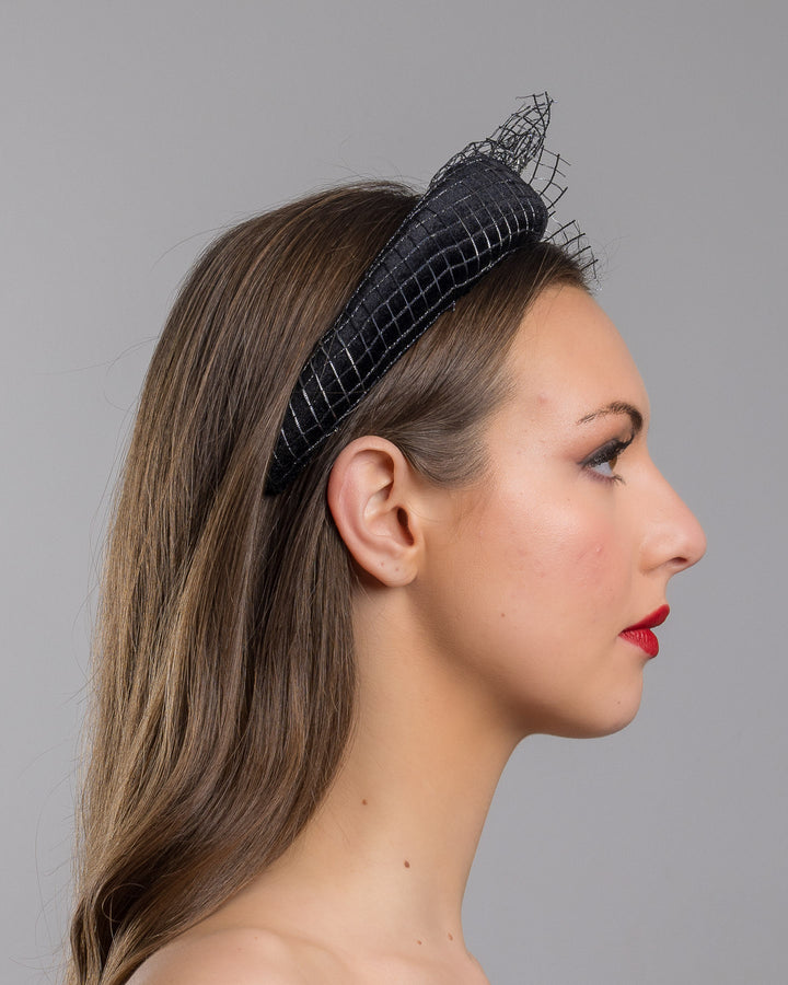Model is showcasing the right side close up of Black Velvet High Headband, covered with a silver black mix net fabric. It is embellished with a net fabric flower and a mother of pearl detailed snail brooch. Made by Merve Bayindir Millinery.