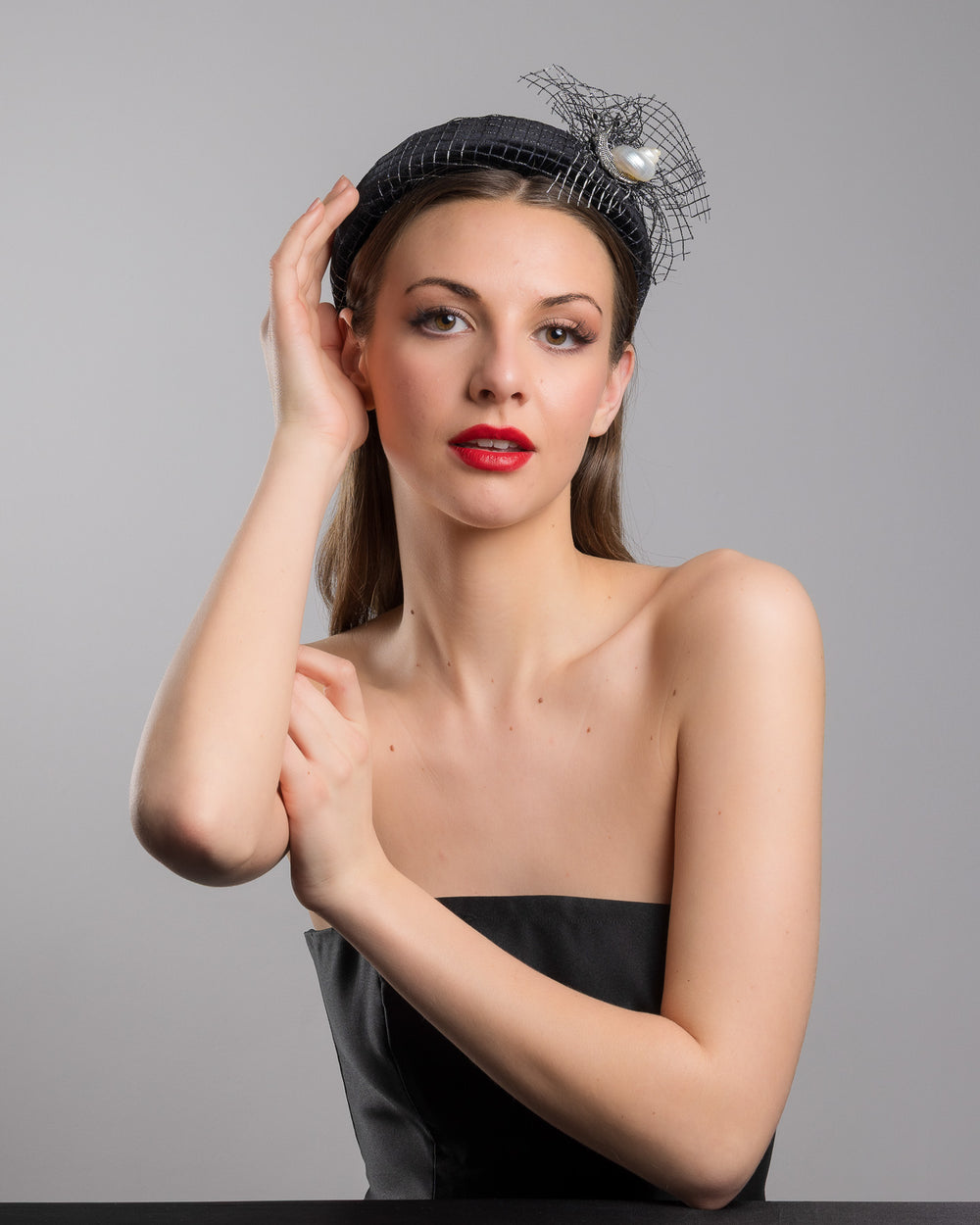 Female model is posing wearing Pearl Snail Black Velvet High Headband, covered with a silver black mix net fabric. It is embellished with a net fabric flower and a mother of pearl detailed snail brooch. Made by Merve Bayindir Millinery.