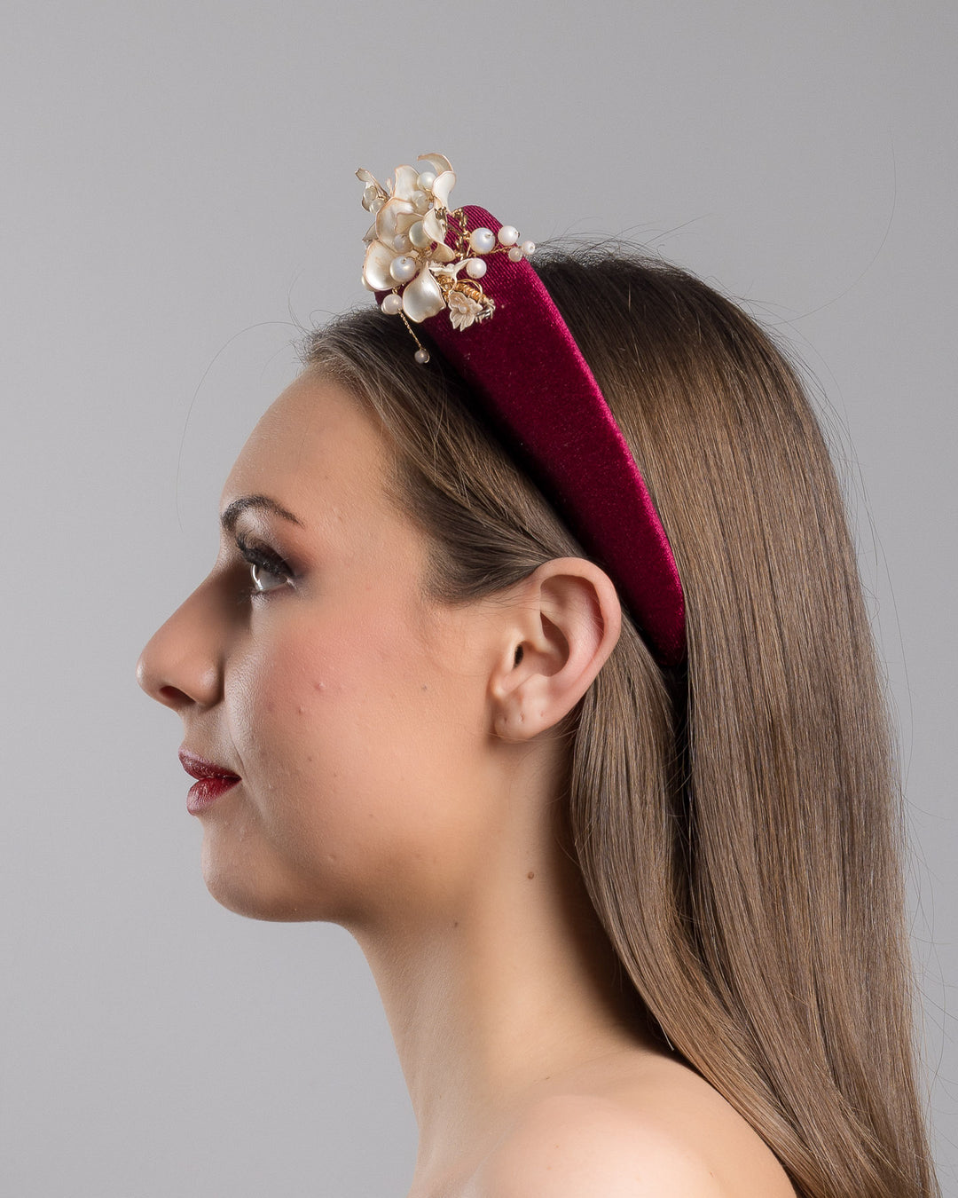 Model is showcasing the left side of the high burgundy velvet headband decorated with pearl coloured wired bead and resin flowers. Made by Merve Bayindir millinery.