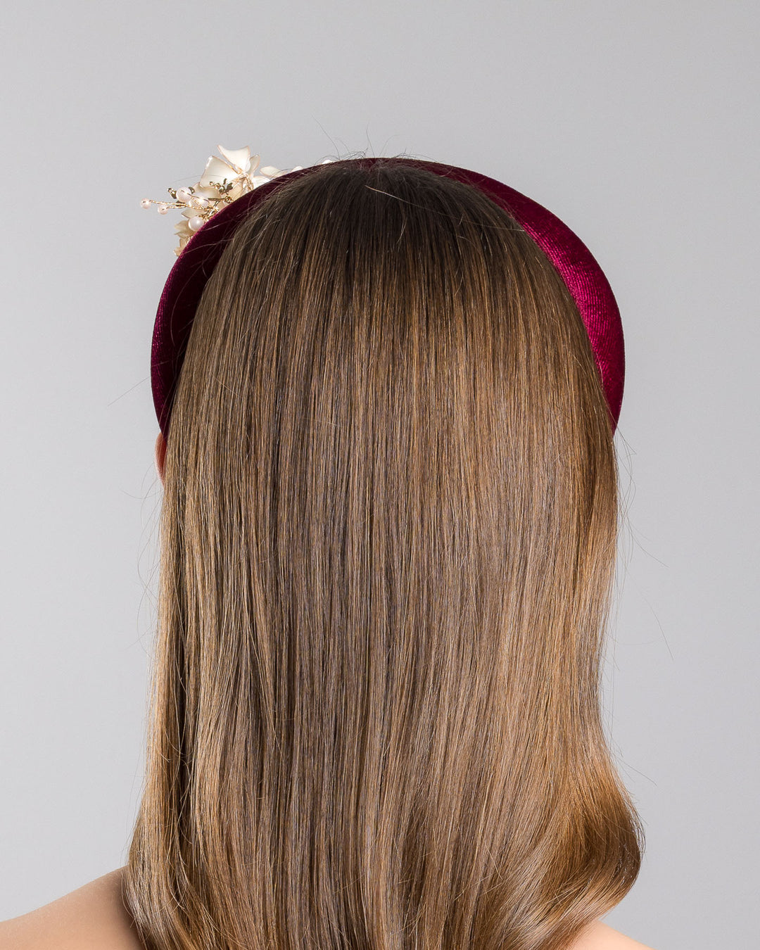 Model is showcasing the back of the high burgundy velvet headband decorated with pearl coloured wired bead and resin flowers. Made by Merve Bayindir millinery.
