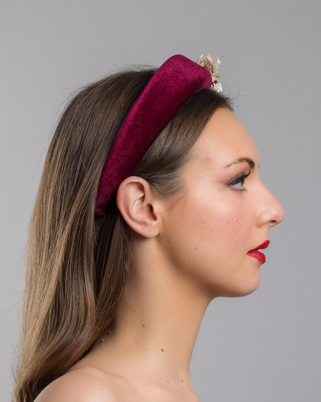 Model is showcasing the right side of the high burgundy velvet headband decorated with pearl coloured wired bead and resin flowers. Made by Merve Bayindir millinery.