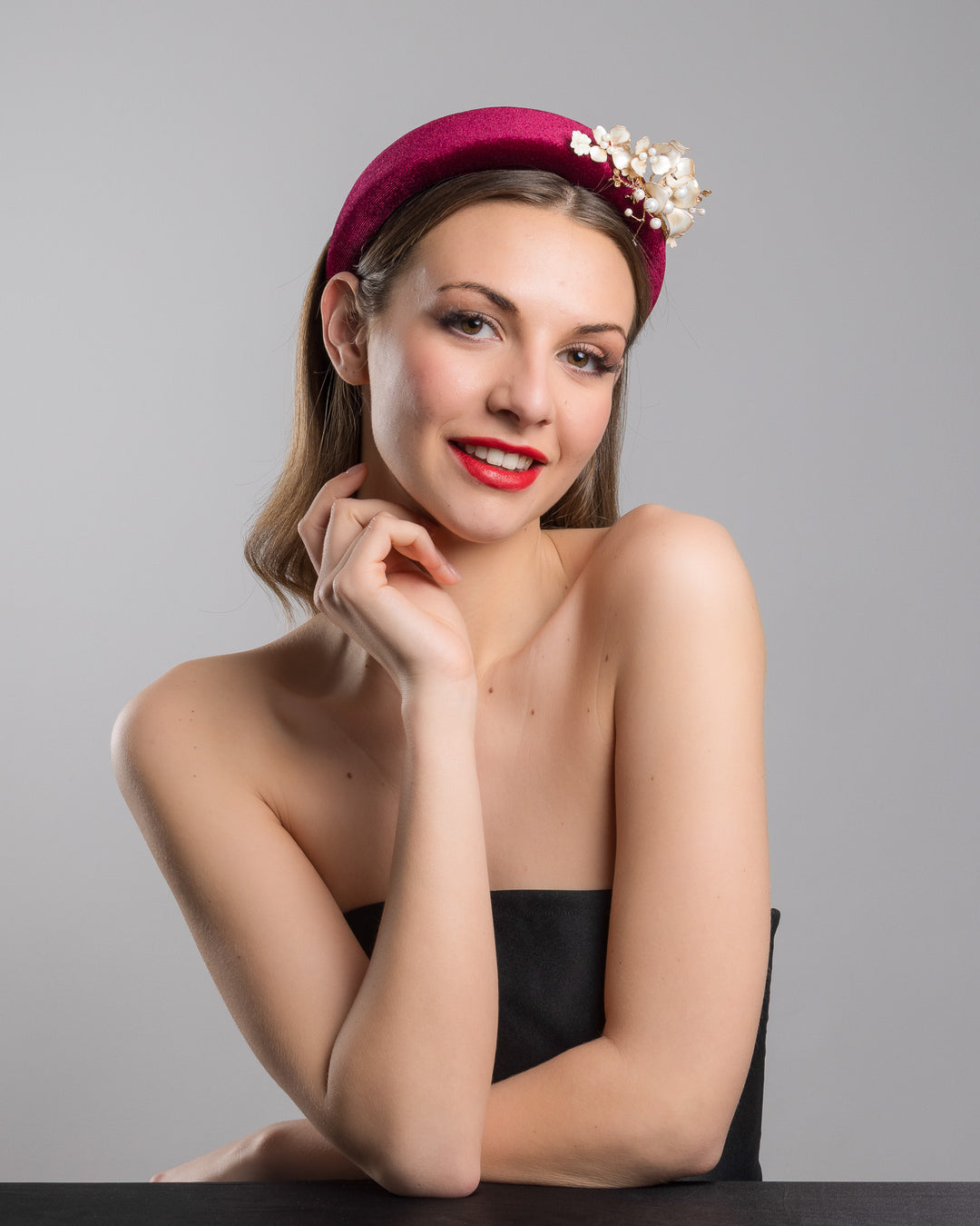 Model is posing wearing the Permissio a high burgundy velvet headband decorated with pearl coloured wired bead and resin flowers. Made by Merve Bayindir millinery.