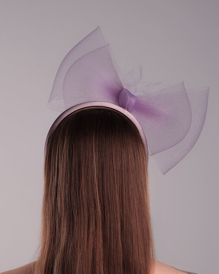 The model is showcasing the back side of a semi high dark lilac silk headband decorated with double layerd large crinoline bow embellished with a silk organza butter