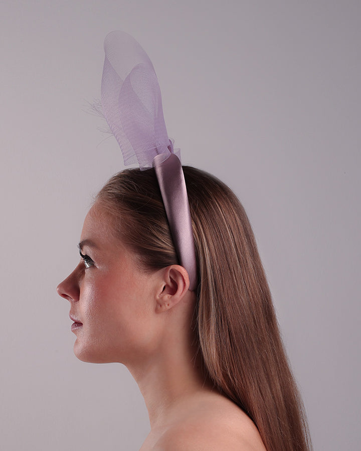 The model is showcasing the left side of a semi high dark lilac silk headband decorated with double layerd large crinoline bow embellished with a silk organza butterfly.