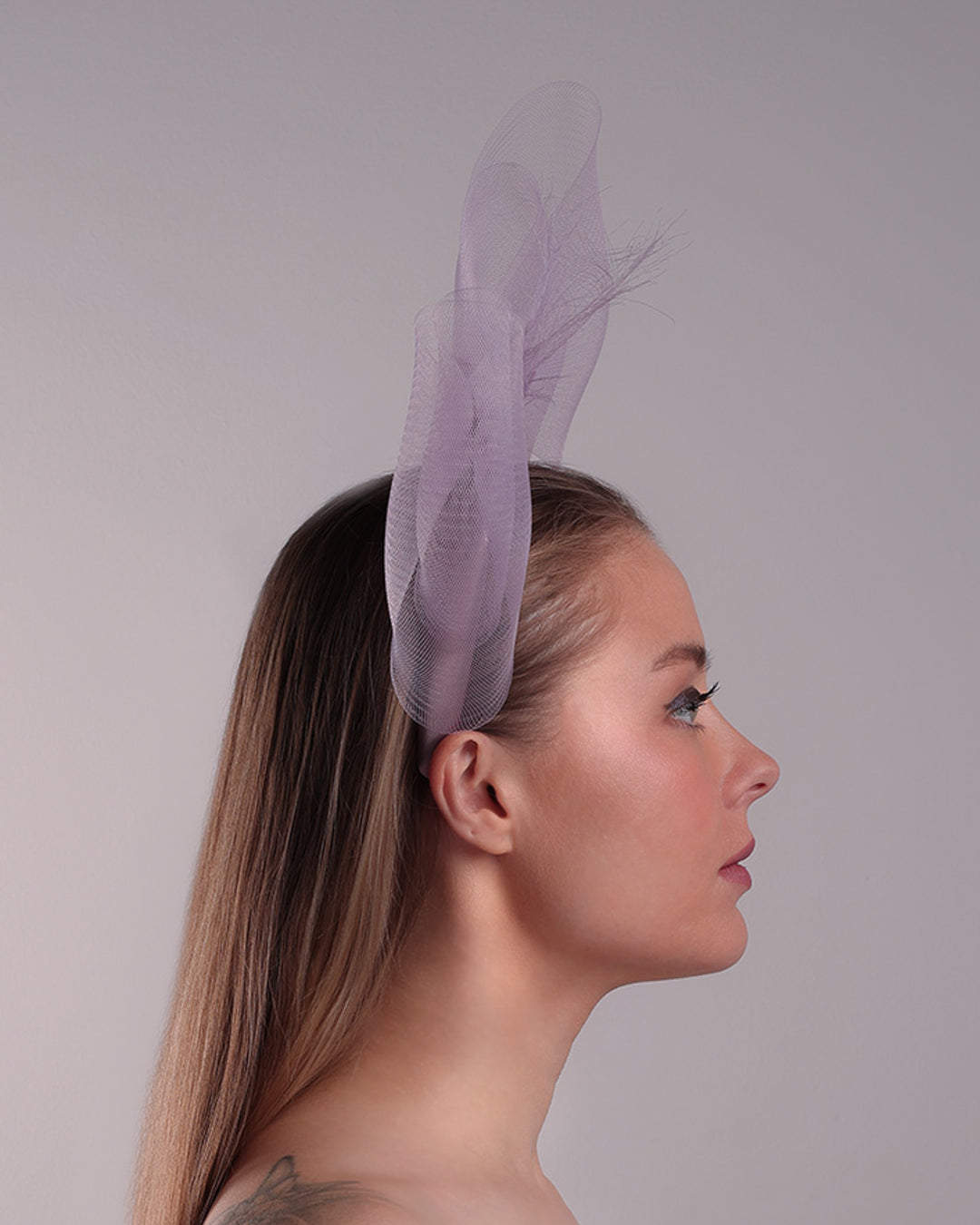 The model is showcasing the right side of a semi high dark lilac silk headband decorated with double layerd large crinoline bow embellished with a silk organza butterfly.