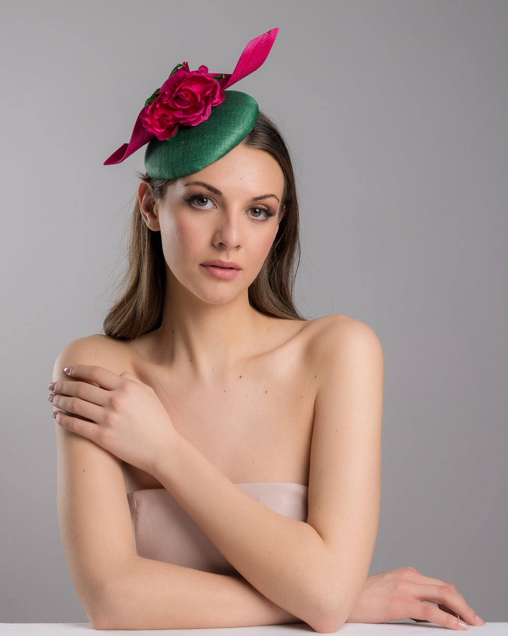 Model is posing wearing the Revel green fascinator with a pink jinsin swirl crossing the base, the centre of the swirls adorned with a hot pink rose. The fascinator sits on the right front side of the head. Designed and made by Merve Bayindir millinery.