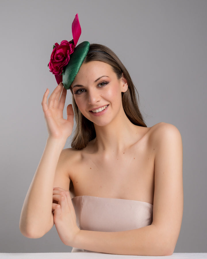 Model is posing wearing the Revel green fascinator with a pink jinsin swirl crossing the base, the centre of the swirls adorned with a hot pink rose. The fascinator sits on the right front side of the head. Designed and made by Merve Bayindir millinery.
