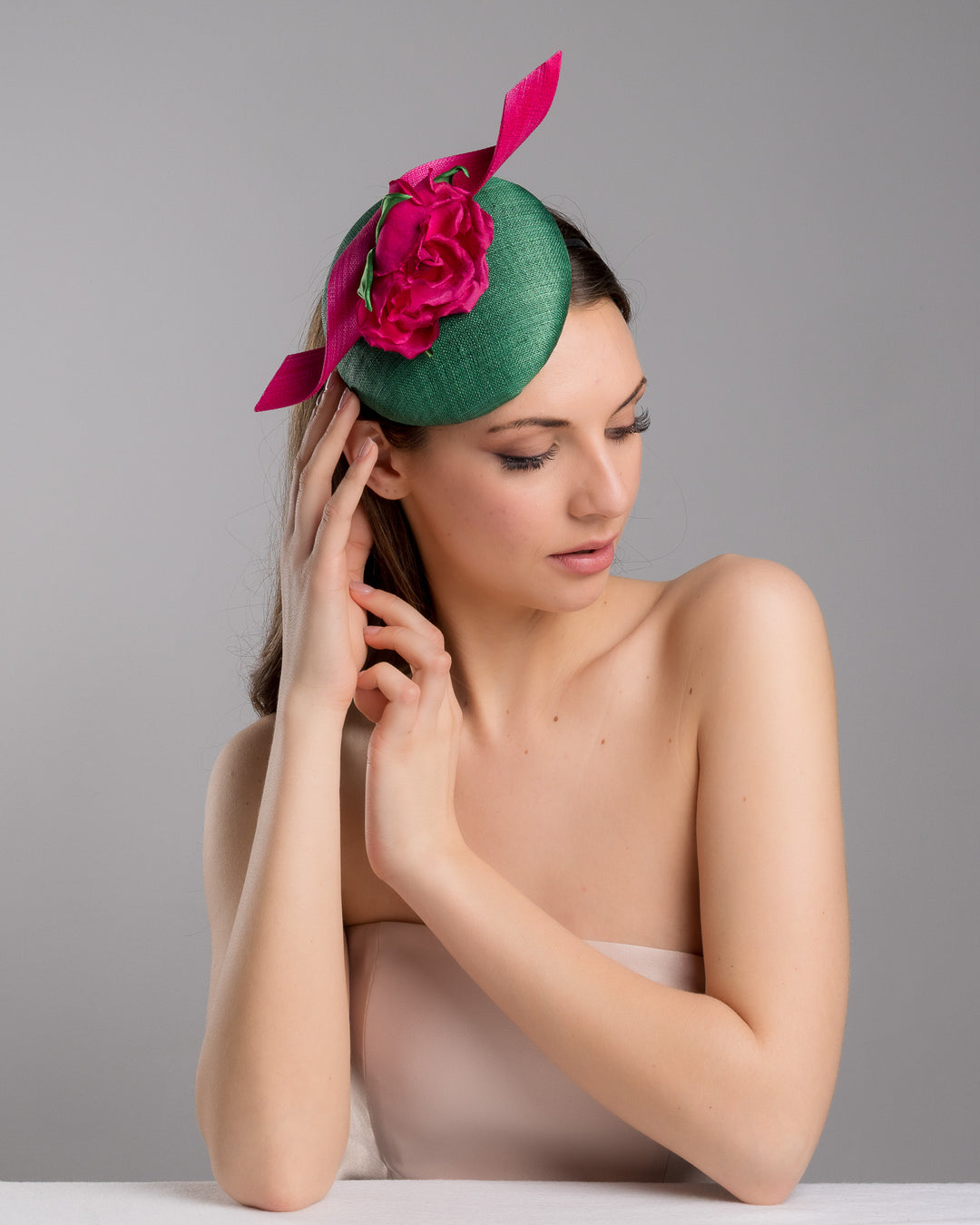 Model is posing wearing the Revel green fascinator with a pink jinsin swirl crossing the base, the centre of the swirls adorned with a hot pink rose. The fascinator sits on the right front side of the head. Designed and made by Merve Bayindir millinery.