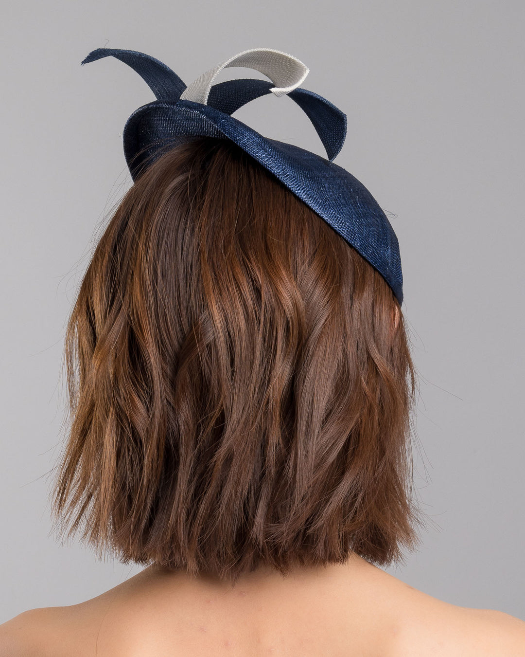 Model is showcasing the back side close up of asymmetric navy saucer, decorated with white and navy buntal swirls and completed with multi coloured crystal beads. The height gained on the left side of this headpiece creates a dramatic effect and completes your style with a unique touch. Designed and made by Merve Bayindir millinery.