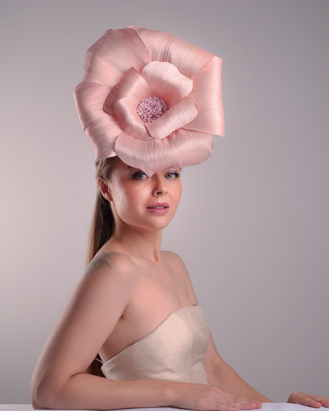 Model is showcasing the right front angle from the side,  of an extra large light pink silk abaca flower centred towards the right side of the head. Fitted on a pink mini saucer style fascinator.