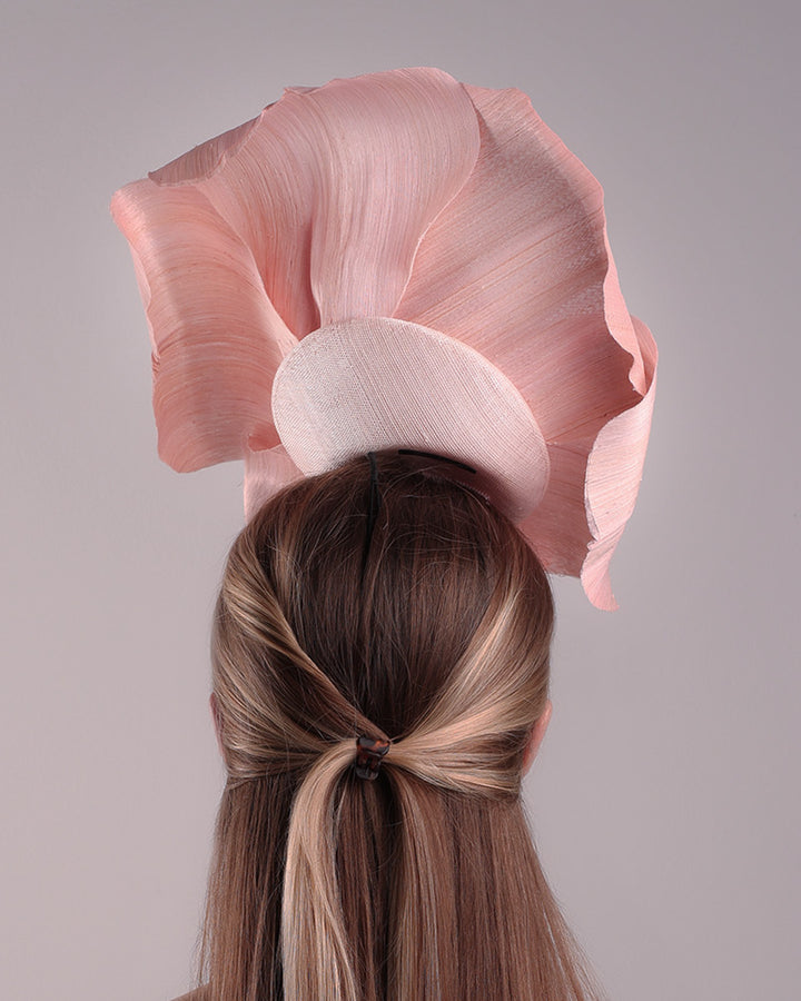 Model is showcasing the back of an extra large light pink silk abaca flower centred towards the right side of the head. Fitted on a pink mini saucer style fascinator.