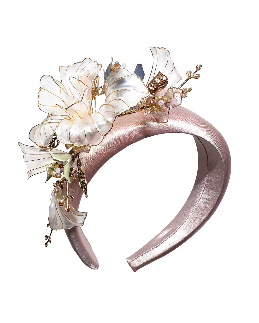 Blush pink satin padded headband featuring sculptural translucent ivory flowers with fine gold edging. The design is accented with delicate metallic leaves, soft blush crystal details, and subtle beadwork arranged asymmetrically along one side, creating an elegant and luminous statement piece suitable for weddings and formal occasions. Designed and made by Merve Bayindir Millinery.
