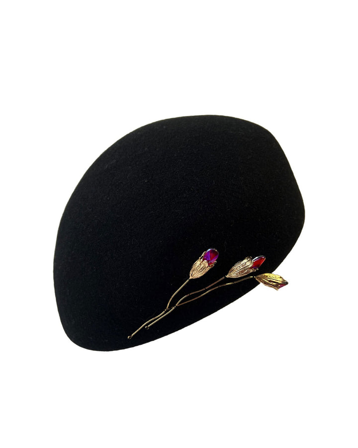 The still life picture of the black wool beret hat is decorated with a real gold-plated brass metal branch motif adorned with crystal-tipped buds. Designed by Merve Bayindir.