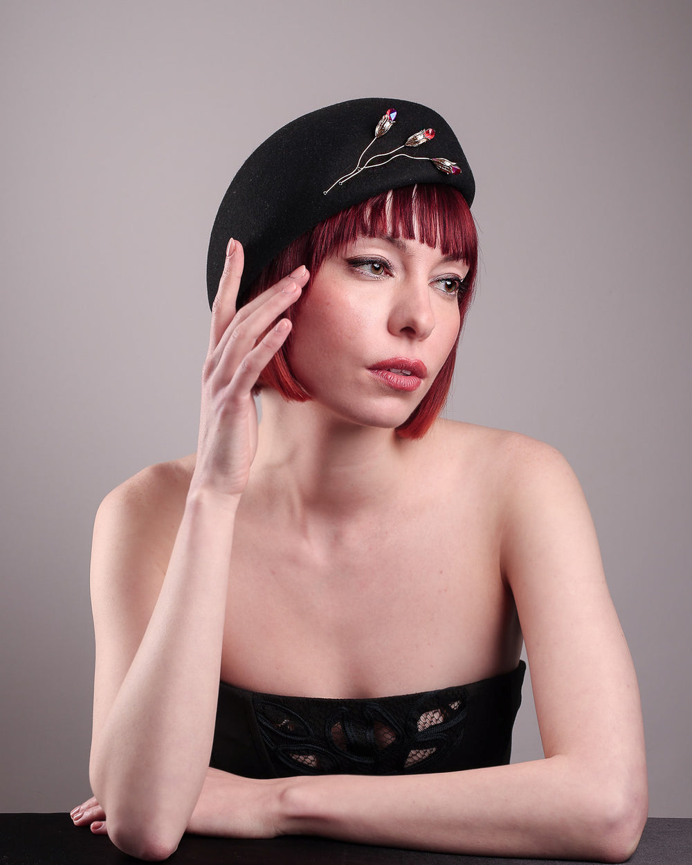 The female model is wearing a wool beret-style hat, showcasing the right front view it. The black hat is decorated with a real gold-plated brass metal branch motif adorned with crystal-tipped buds. The side beret is higher on the left side and shorter on the right side, and is suggested to be worn tilted. Designed by Merve Bayindir.